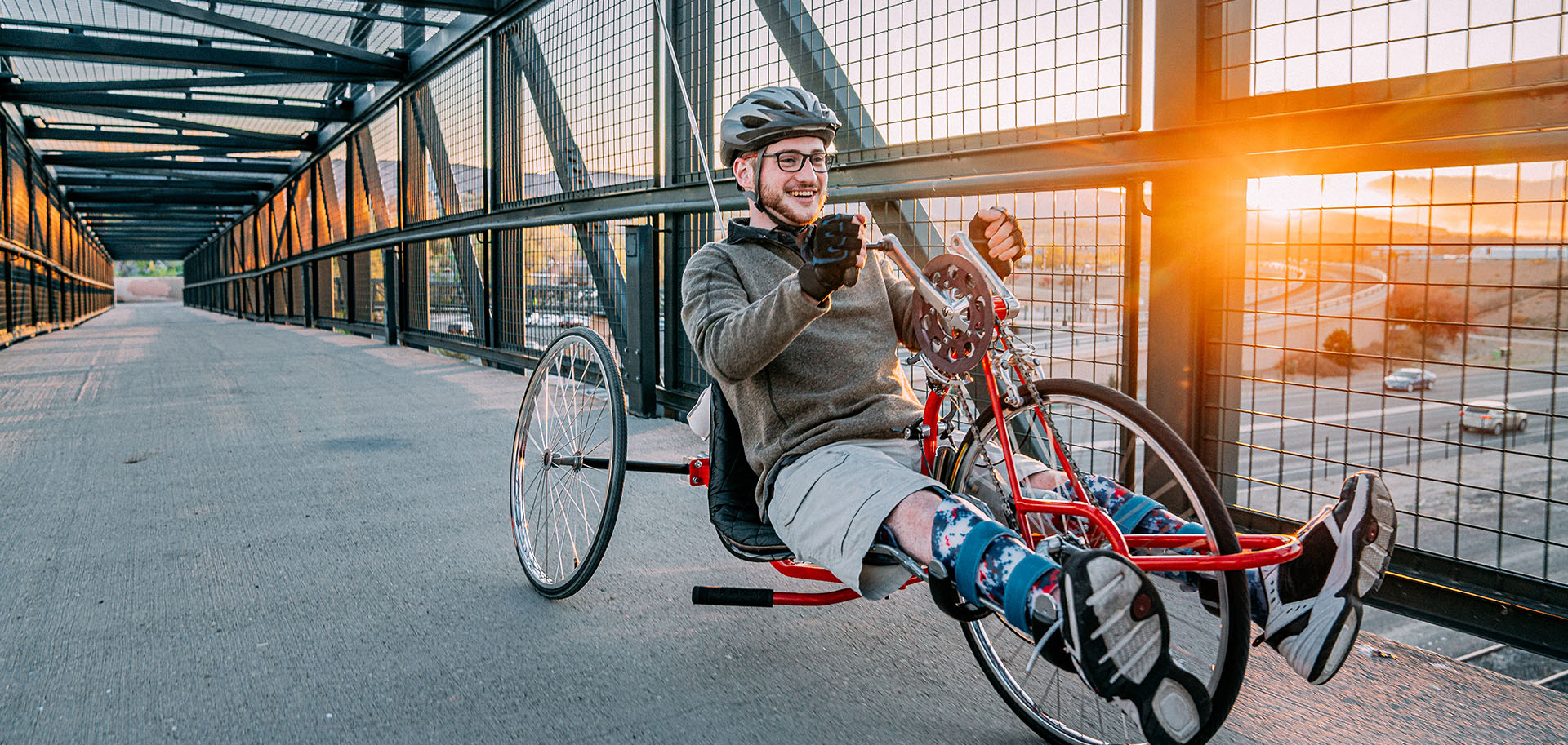 Handsome Young Man with Myelomeningocele Spina Bifida Riding a Red Handcycle Wearing Orthotic Leg Braces for Adaptive Exercise Outdoors in the Spring. Overcoming the Stigma and Challenges of Disability can be Fun on a Hand bike!
