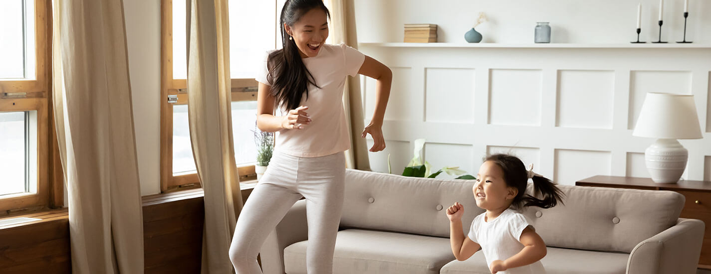 A mother and young daughter are dancing in their living room.