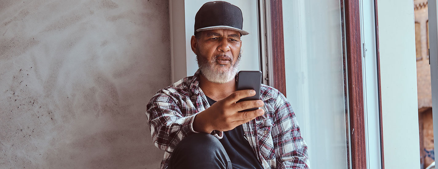 A middle aged man is sitting in a window seat, looking at his phone trying out the new digital diabetes prevention program.